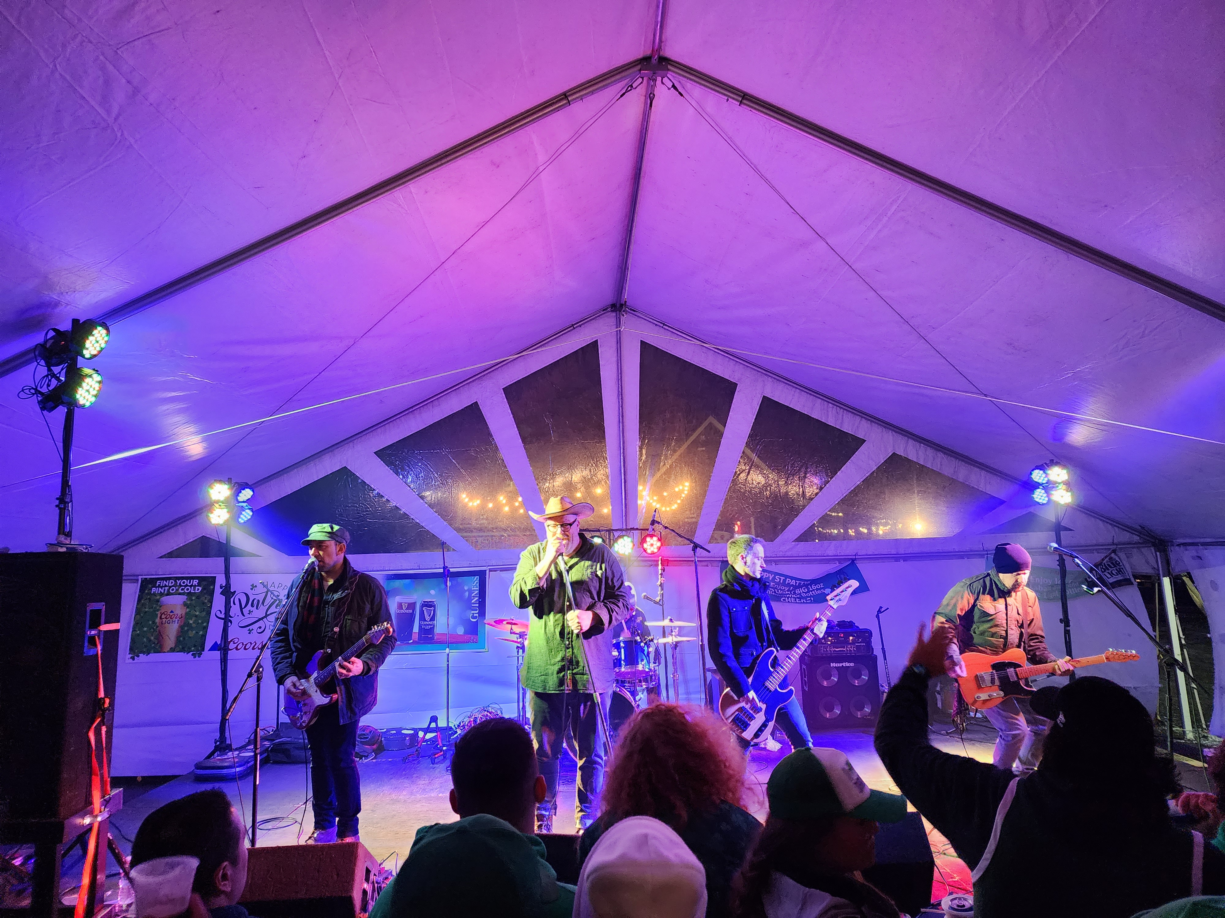 four musicians perform on stage inside a large tent with a crowd below them