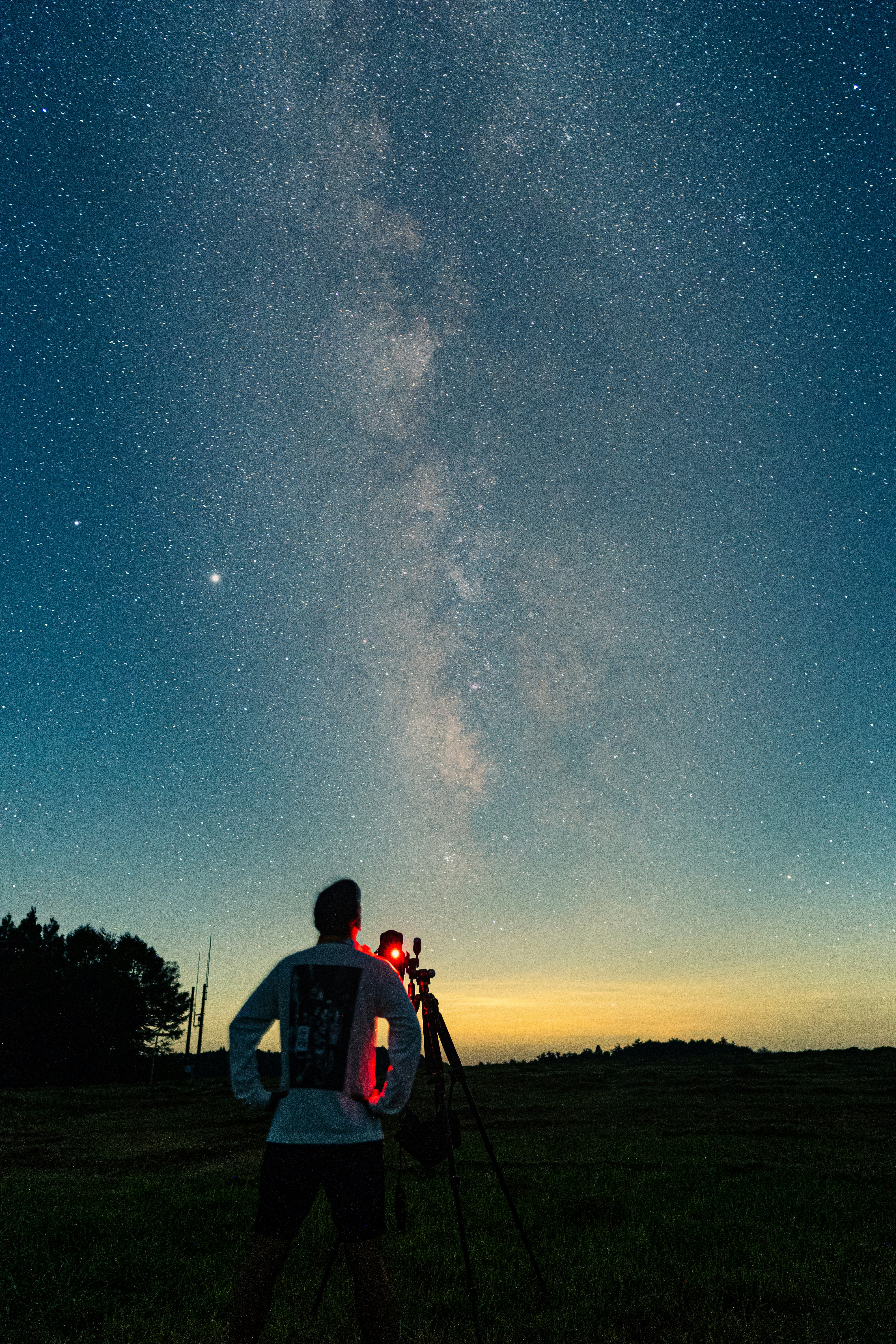 Man stands behind telescope viewing the sky at dusk