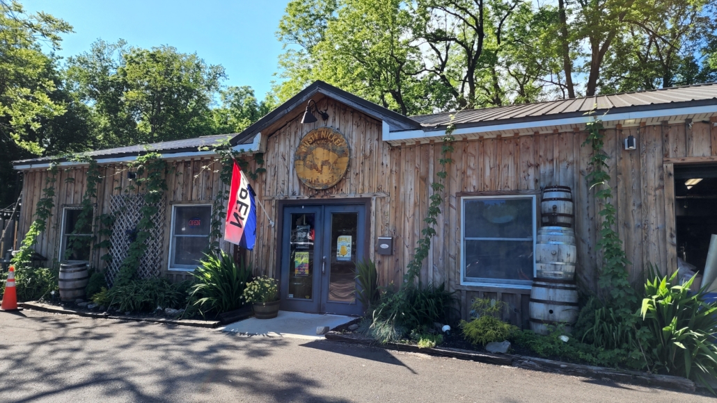 Exterior image of the front entrance to Rusty Nickel Brewing's Tasting Room and Brewery. The one-story building has wood siding.