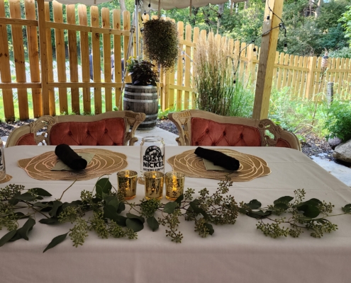 An overhead view of a sweetheart table. Two place setting are set behind greenery and tea light candles. Two vintage chairs with velvet cushions sit empty behind the table.