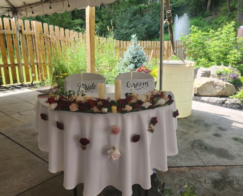 A sweetheart table is decorated with flowers and candles. Signs for "bride" and "Groom" are hung on the chairs.