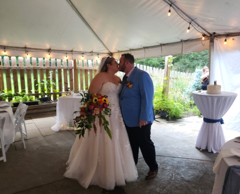 A bride and groom share a kiss under the large white tent. The bride is holding a large bouquet.