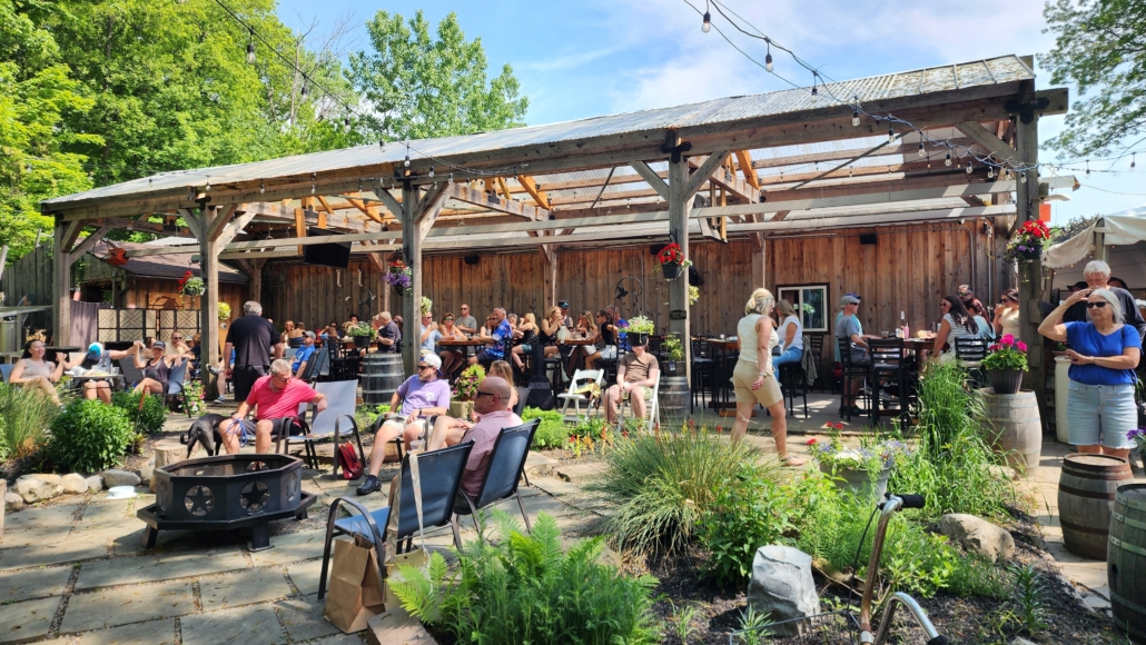 The beer garden at Rusty Nickel Brewing. Guests are seated outside surrounded by garden beds and plants. The large timber pergola with a roof can be seen in the background.