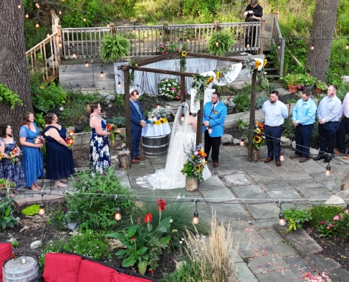 An aerial view of a wedding ceremony in the beer garden. A bride and groom stand under a chuppah with their bridesmaids and groomsmen standing to either side of them