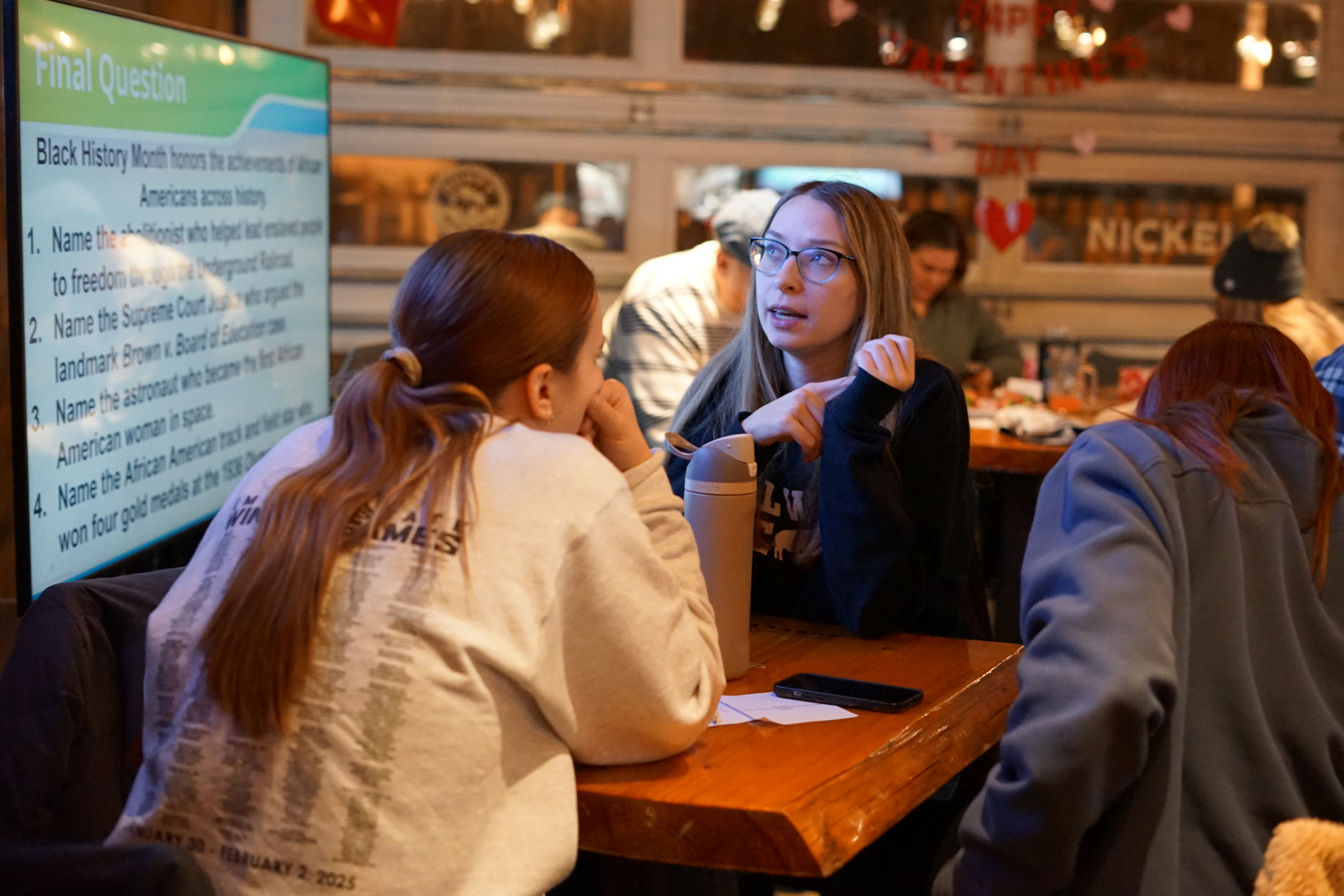 Two women discuss possible answers during a Trivia Night