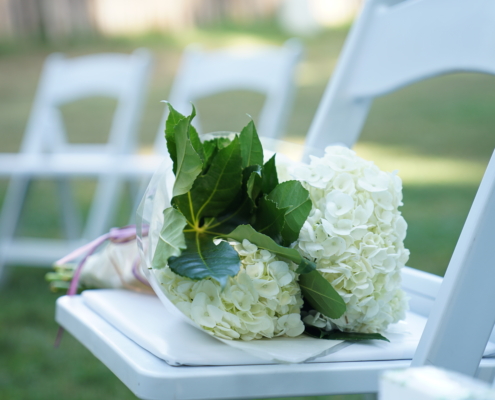 a bouquet of hydrangea flowers rests on a chair at a wedding ceremony