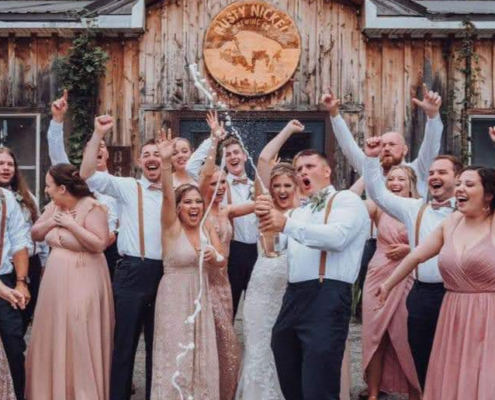 a wedding party cheers as a groom sprays a bottle of champagne alongside his bride.