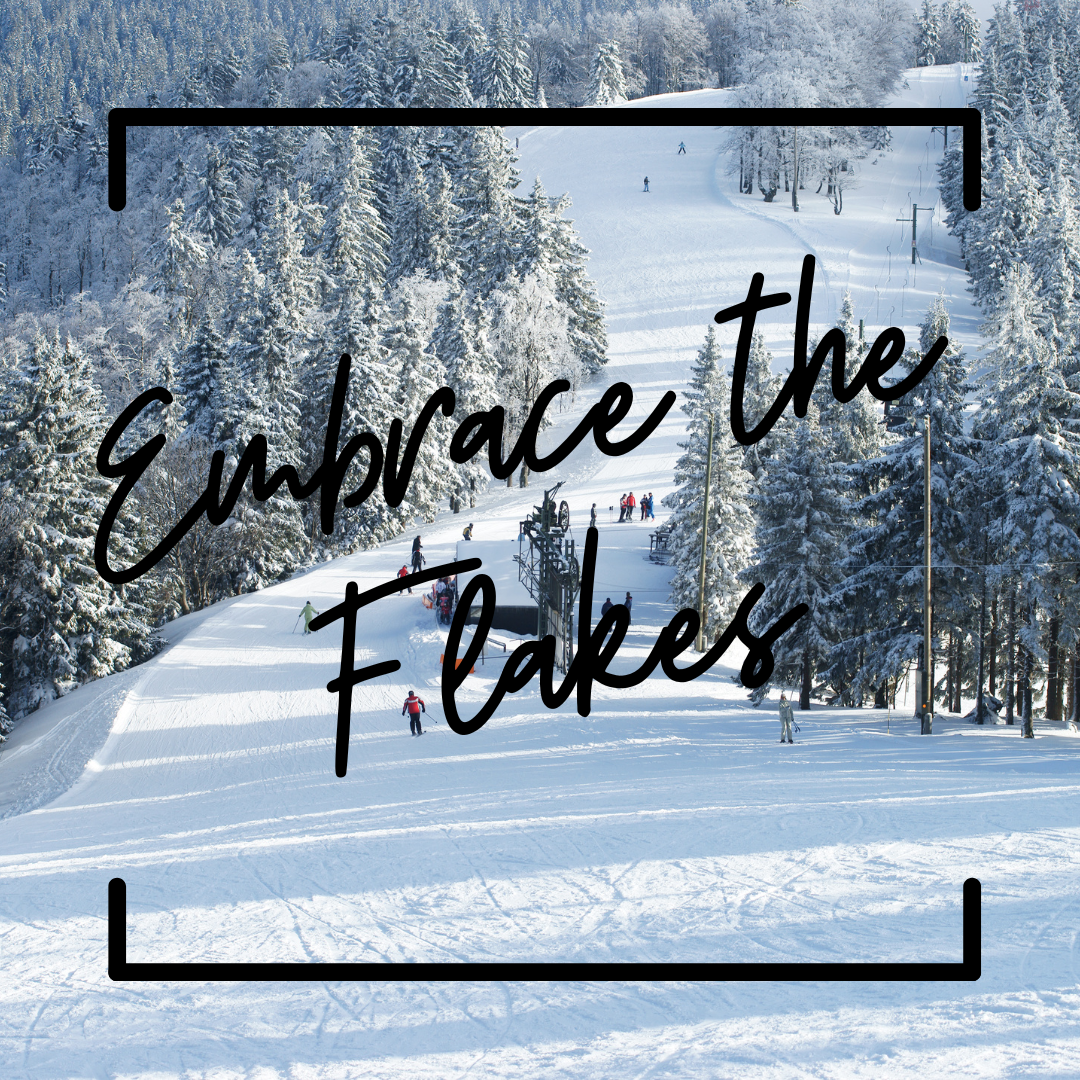 A snowy ski hill surrounded by frost covered pine trees. The text reads "embrace the flakes"