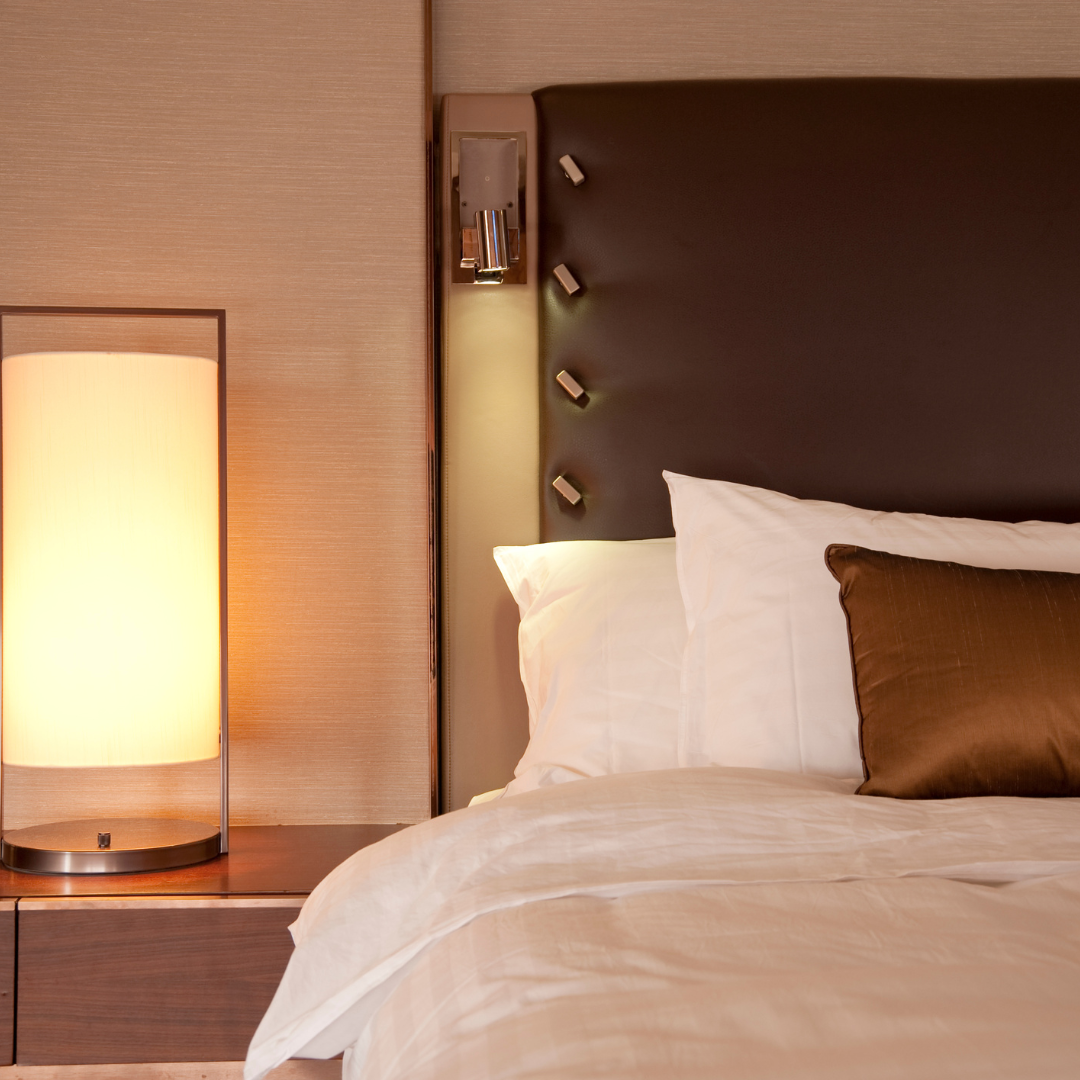 a hotel bed is neatly made with a leather headboard and lamp on the side table