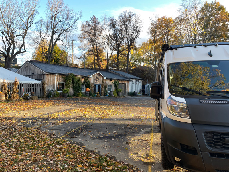 An autumn scene at Rusty Nickel Brewing. Fallen leaves cover the parking lot, haybales and pumpkins can be seen in the front gardens. A sprinter van is parked in the lot