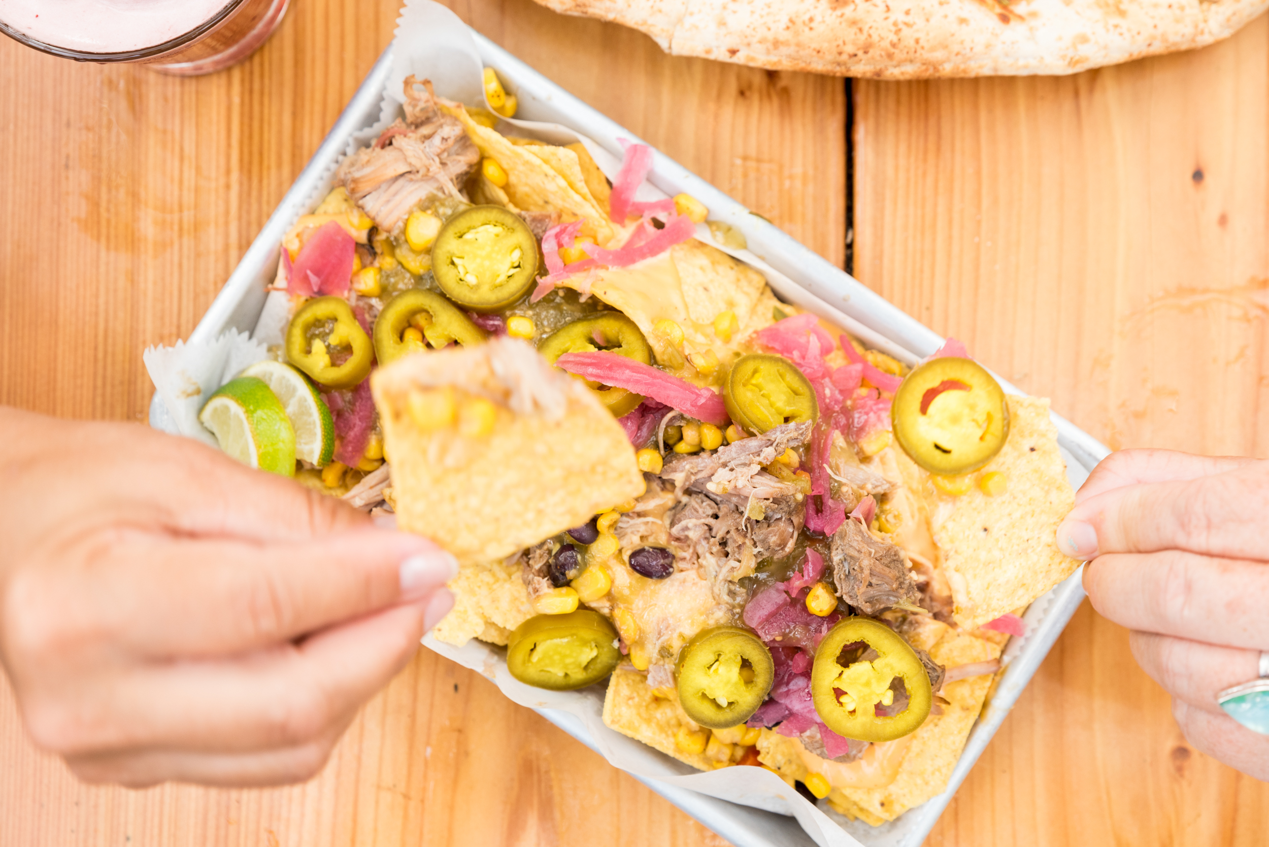 SOB-RustyNickel-080525-Selects-34 a guest holds a tortilla chips above a tray of nachos loaded with pork carnitas